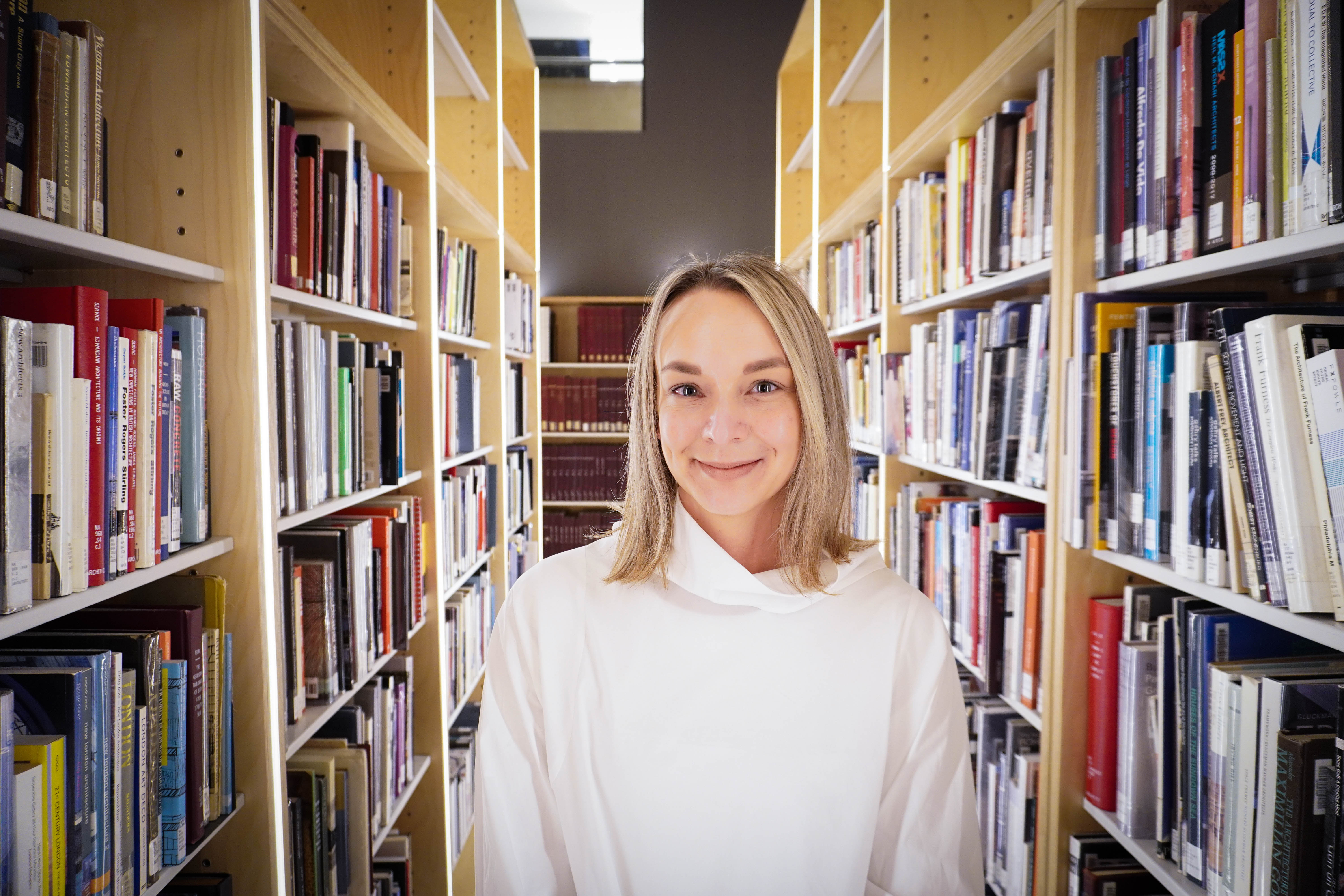 Cathryn Copper standing between rows of bookshelves in the stacks collection area in the Eberhard Zeidler library.